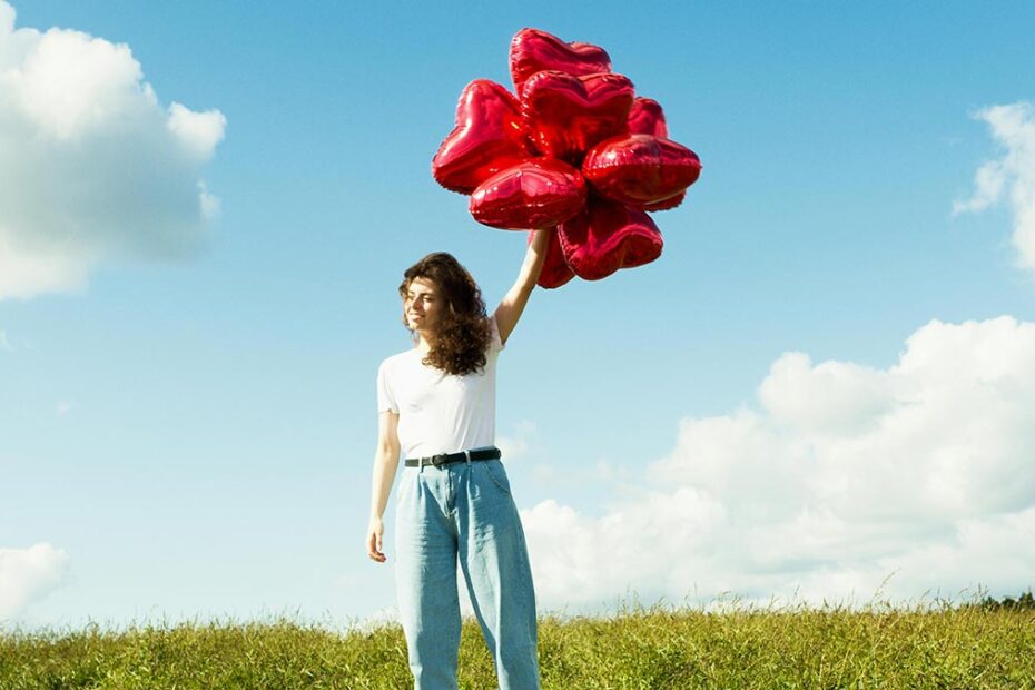 Woman holds bunch of heart shaped balloons against a blue sky