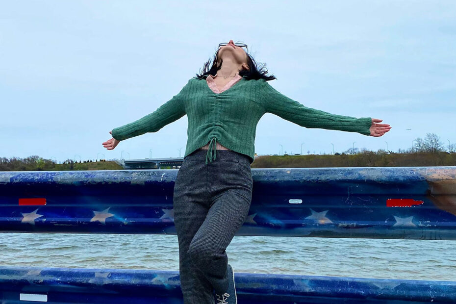 Experiencing the freedom of accepting and letting go - woman leaning back against a railing by the see, arms outspread and gazing at the sky